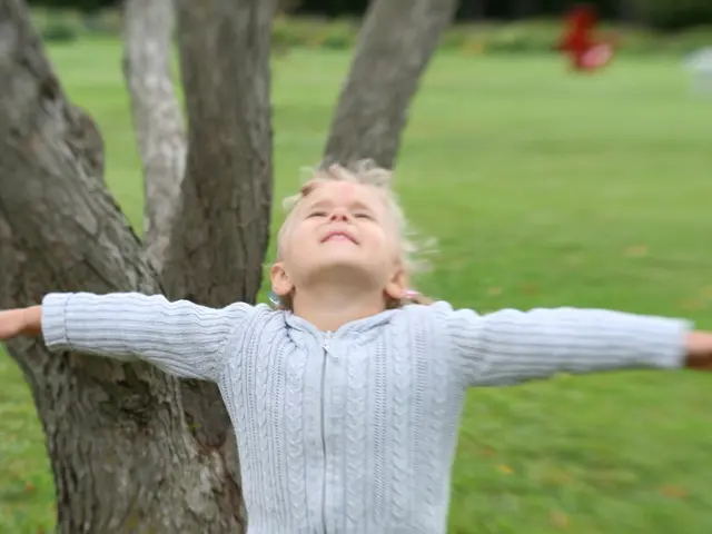 There is a child in jean pant, stretching his both hands and standing on an yellow color object. In...