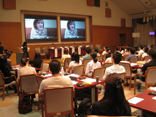 There are two screens in which a woman is placed and talking. Behind that there is a table and...